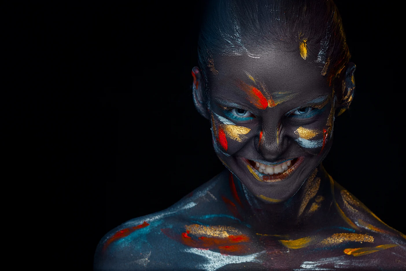 Portrait artistique : un visage souriant peint en noir avec des touches d’or, de rouge et de bleu